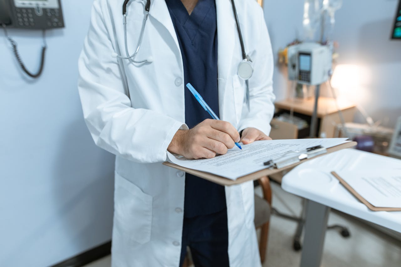 A doctor in a lab coat writing notes in a hospital setting, using a clipboard.